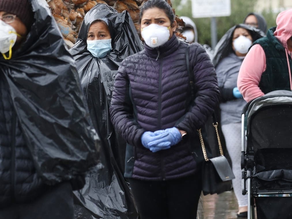 VAN NUYS, CALIFORNIA - APRIL 09: Juana Gomez (2nd L), from North Hollywood, wears a face mask, while using a trash bag to protect against the rain, as she waits in line to receive food at a Food Bank distribution for those in need as the coronavirus pande