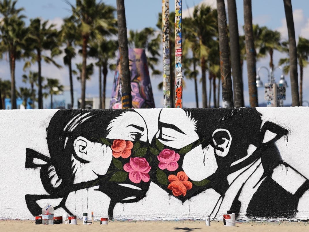 Palm trees stand behind a street art piece by artist Pony Wave depicting two people kissing while wearing face masks on Venice Beach on March 21, 2020.