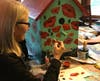 Artist Sue Hoy in the process of painting her little library that is adorned with vibrant poppy flowers.