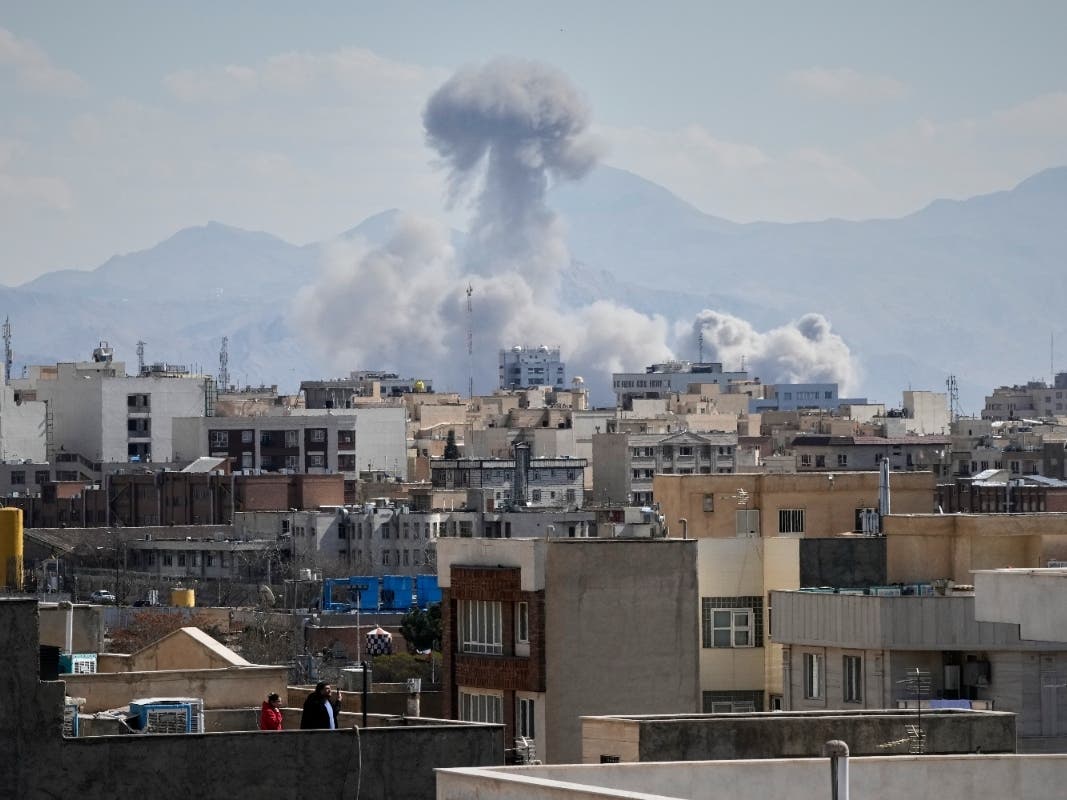 People watch from a rooftop as a plume of smoke rises after a strike in Tehran, Iran, Sunday, March 1, 2026.