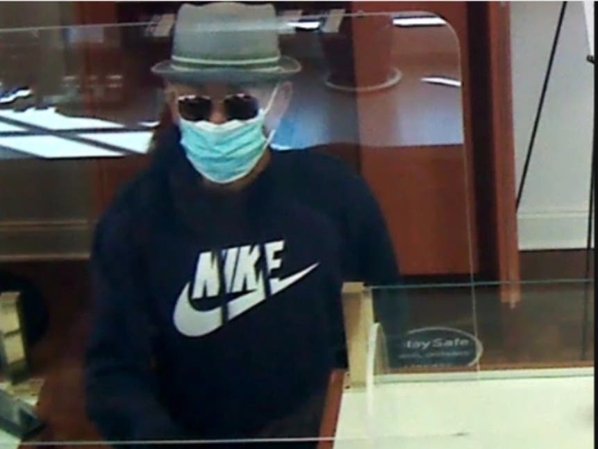 Wearing a dark blue Nike hooded sweatshirt, black sweatpants, dark-colored shoes, blue face mask, brown-framed sunglasses, and a fedora, he walked into the bank and passed a note to a teller demanding money and warning them not to activate the alarm.
