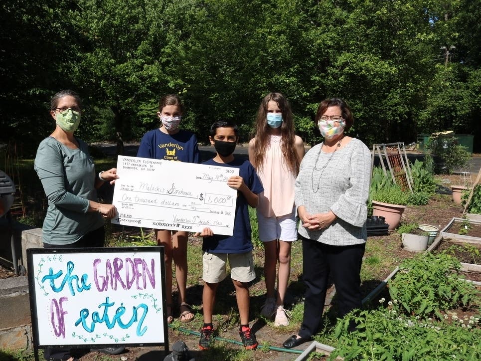Malachi’s Storehouse Director Judi Carlson (l) and Dunwoody Mayor Lynn Deutsch accept Vanderlyn Elementary’s 5th Grade Class gift @ $1,000 in St. Patrick’s “Garden of Eaten”