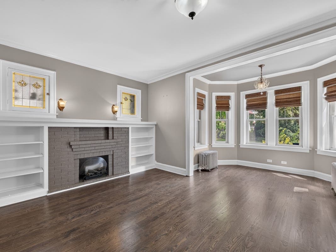 The gracious living room at 845 S Humphrey Ave #1 features original built-ins and art glass, a decorative fireplace, brand-new oak hardwood floors and an adjoining east-facing sunroom filled with natural light.