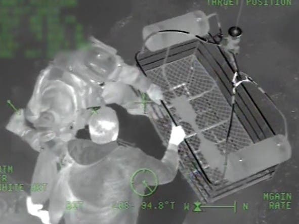 A Coast Guard rescue swimmer helps a stranded boater into a rescue basket lowered from a MH-65 Dolphin helicopter