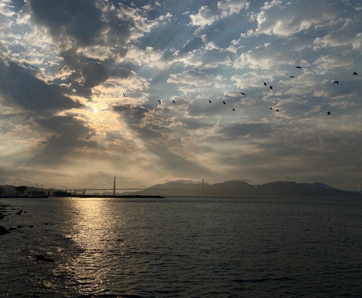 Sunbeams streak from behind clouds, with the Golden Gate Bridge and Marin Headlands in the distance.