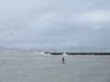 As one person enjoys a water craft, other walk on the Rock Wall as waves crash against it in Alameda, Calif.