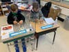 Students constructing a two-story structure using mini marshmallows and toothpicks before placing the structure in a tin filled with ping pong balls or Jell-O, then simulated an earthquake by moving the tin