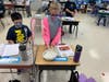 Students constructing a two-story structure using mini marshmallows and toothpicks before placing the structure in a tin filled with ping pong balls or Jell-O, then simulated an earthquake by moving the tin