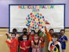Students in Ms. Nunez's first grade class stand in front of the colorful multicultural day bulletin board with flags that represent their heritage.