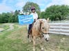 Andove resident Vicky Bernard, longtime board member and volunteer at Challenge Unlimited at Ironstone Farm, holds a sign announcing that the Andover nonprofit has received a three-year, $100,000 Cummings Grant. 