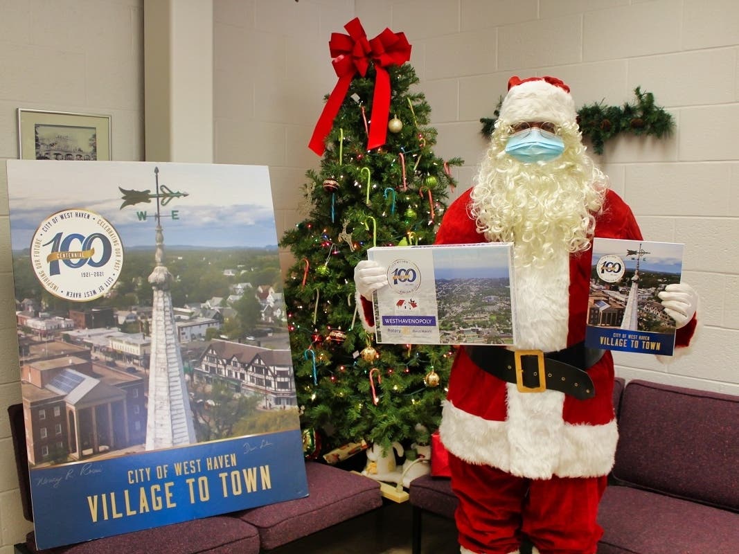 Santa Claus, West Haven’s supreme history buff, holds a paperback copy of the new centennial book, “City of West Haven: Village to Town,” and WestHavenOpoly, the centennial version of the board game Monopoly, at City Hall on Friday.