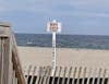 A "beach closed" sign is right at a beach entrance that is blocked by snow fencing. Beach towns are grappling with what to do to convince people to stay out of the water. 