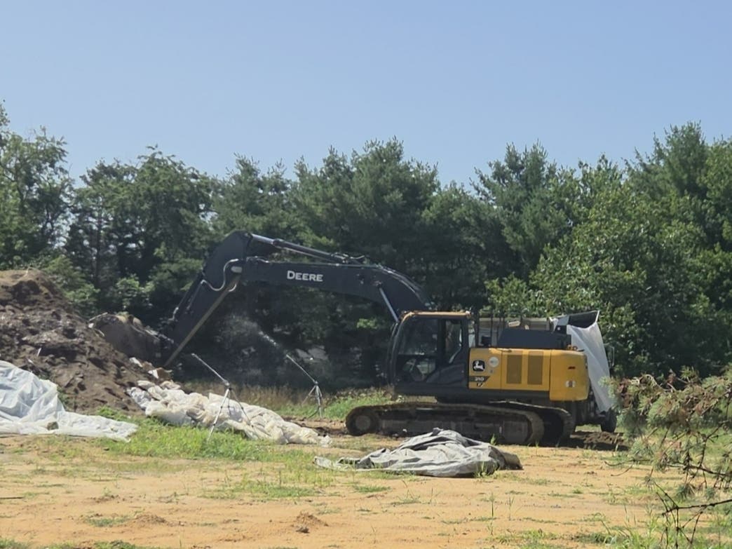 An excavator fills a plastic-lined dump truck with soil at the Clifton Avenue site on Monday for removal to a site licensed to accept asbestos-contaminated soil.