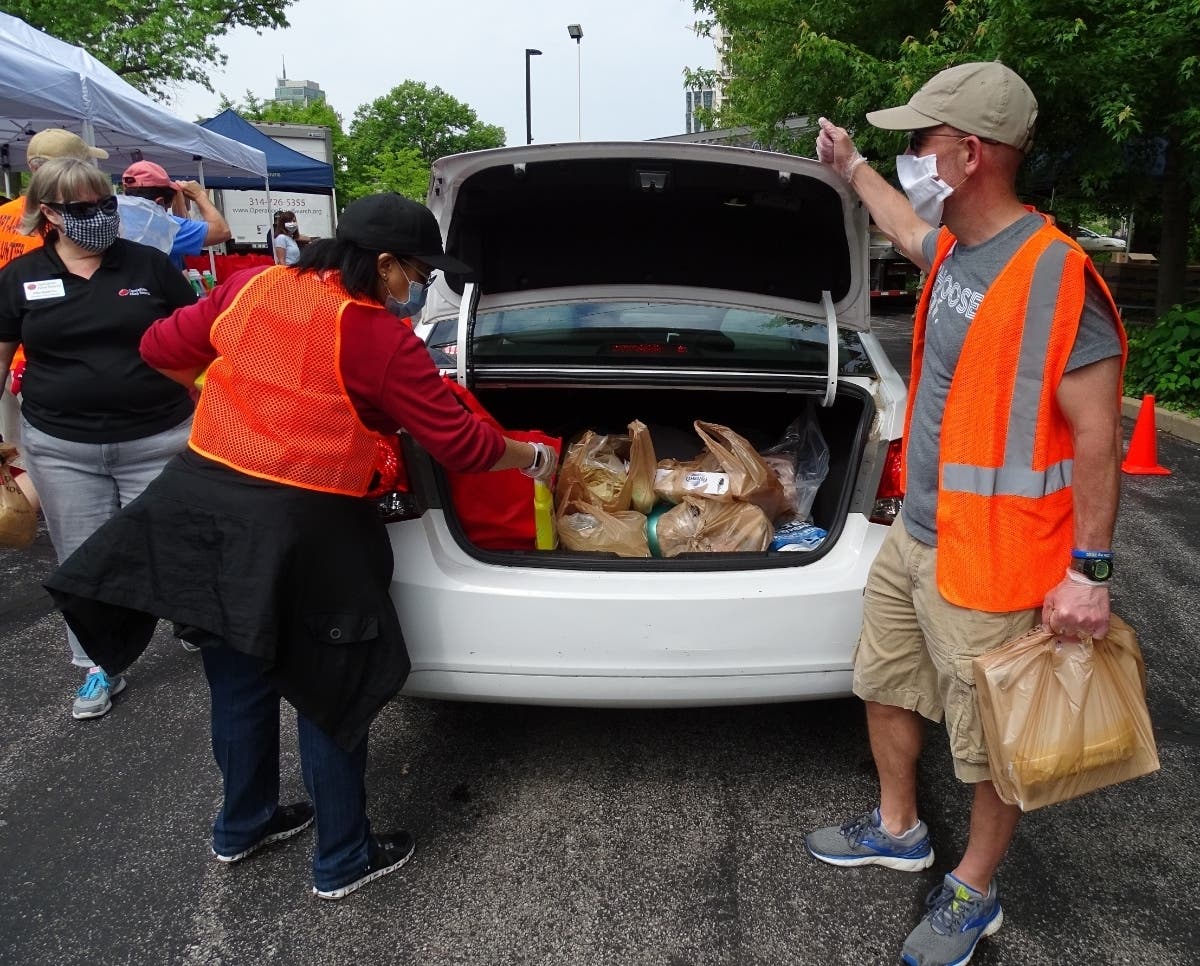Pictured from left to right are Catholic Charities of St. Louis board member Kathy Surratt-States and supporter Gerard Hempstead placing food and supplies into the trunk of a drive-through distribution participant's car.