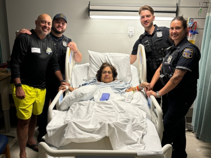 Police officers pose for a photo in the hospital with Devyani Shroff of New Jersey after responding to her home on a medical call, likely saving her life.