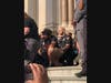 A Jersey City police officer kneels on the steps of City Hall.