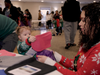 A toddler helps her mom load a bag with a warm winter hat inside the Harmon Cove clubhouse on Dec. 17.