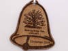 An anniversary keepsake in the shape of a bell, has an image of the Oak Tree and "Christmas 2019" laser etched into the wood.
