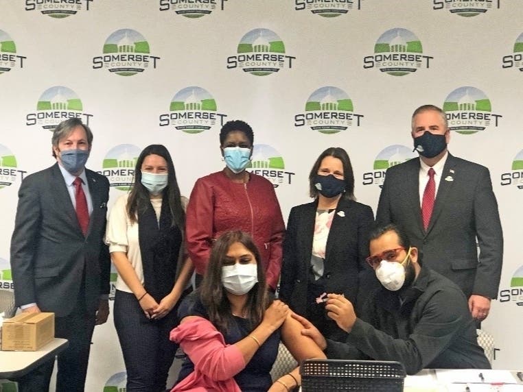 Dr. Namitha Reddy receives the vaccine. Also pictured, Ravi Modh administering the shot, and Somerset County’s (l-r) Freeholder Brian Levine, Deputy Director Sara Sooy, Director Shanel Robinson, Freeholder Melonie Marano, and Freeholder Brian Gallagher.