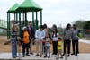 Flanked by park visitors and officials, child helps council member Greg Casar cut the ribbon at St. John Park.
