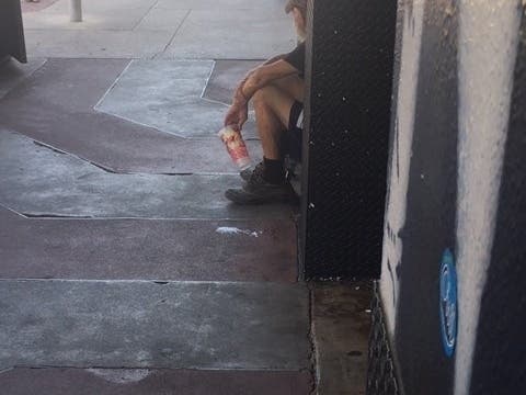 A homeless man finds shade while panhandling along Guadalupe Street across from University of Texas at Austin this summer.
