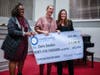 Veteran Milken Educators Amara Alexander (AL '16, left) and Rachel Tommelleo (DC '18, right) give recipient Claire Smullen (DC '19) a hand with her oversized $25,000 Milken Educator Award check. 
