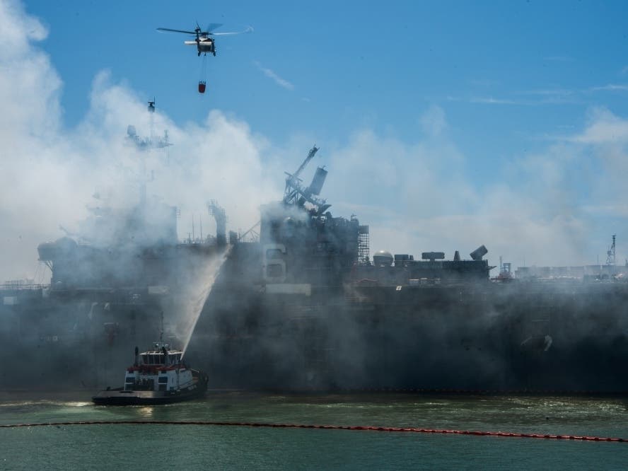 An MH-60S Seahawk helicopter from the “Merlins” of Helicopter Sea Combat Squadron (HSC) 3, provides aerial firefighting support alongside Sailors and civilian fire crews on the ground to fight the fire aboard amphibious assault ship USS Bonhomme Richard.