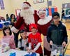 A group of children help Santa and Mrs. Claus pack “Blessing Bags” for the homeless at the 2022 NSYMCA Holiday Giveback Event at the NSYMCA.