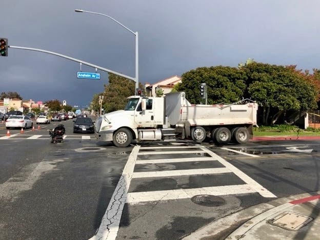 A dump truck strikes two in a Costa Mesa crosswalk, destroying a man's wheelchair and injuring another.