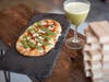 The Not Your Nonna's flatbread features marinara, fior di Latte, Basil Pesto, and a white balsamic Reduction. The Jiminy cocktail is made with gin, matcha honey syrup, elderflower, and lemon.