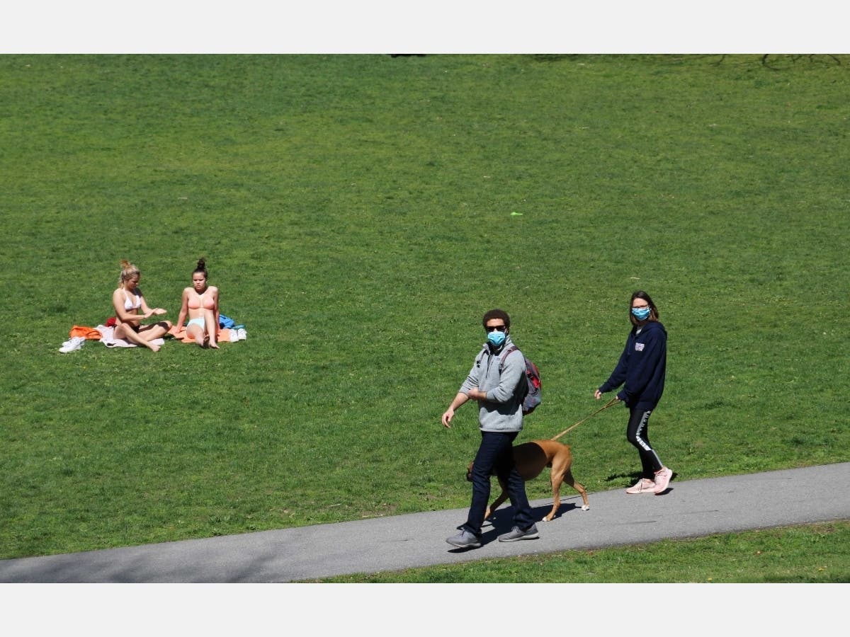 Two women without masks sun themselves in the Boston area on Saturday as to masked pedestrians pass by. 