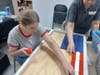 A DoodleBug Workshop participant and a volunteer assemble the pieces for a large wooden American Flag, a popular DoodleBug product which is also available in a smaller size.  The pieces were sanded and painted by other Workshop participants.
