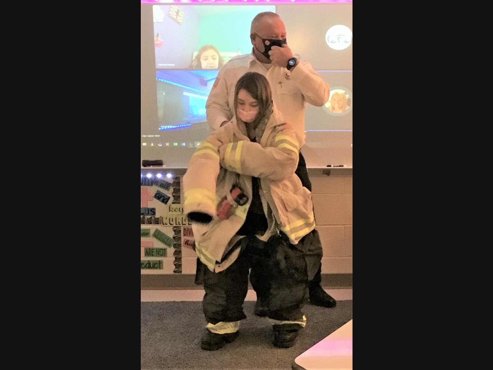 Joliet Fire Chief Greg Blaskey helps Troy Heritage Trail Elementary School student Madison  try on firefighter gear.