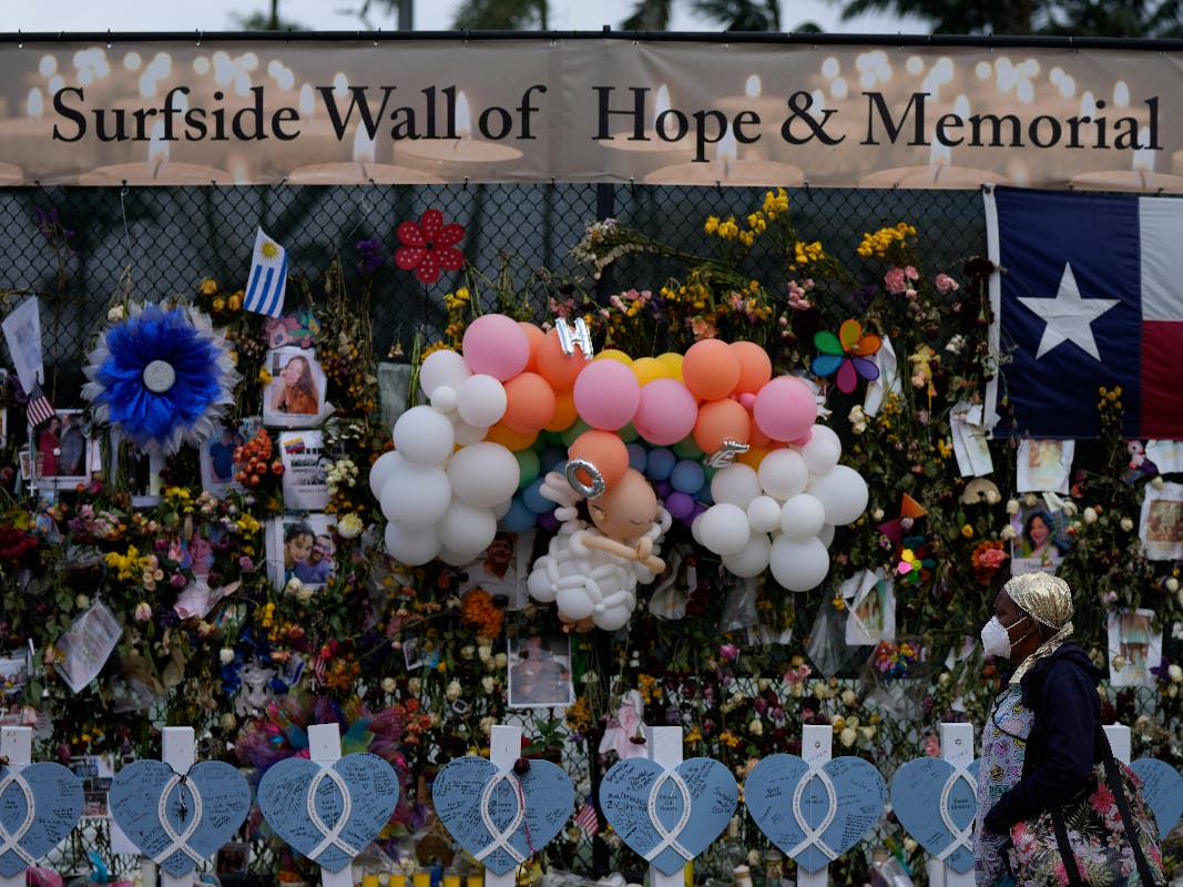 A woman walks past a makeshift memorial for the victims of the Champlain Towers South building collapse, on Monday, July 12, 2021, in Surfside, Fla.
