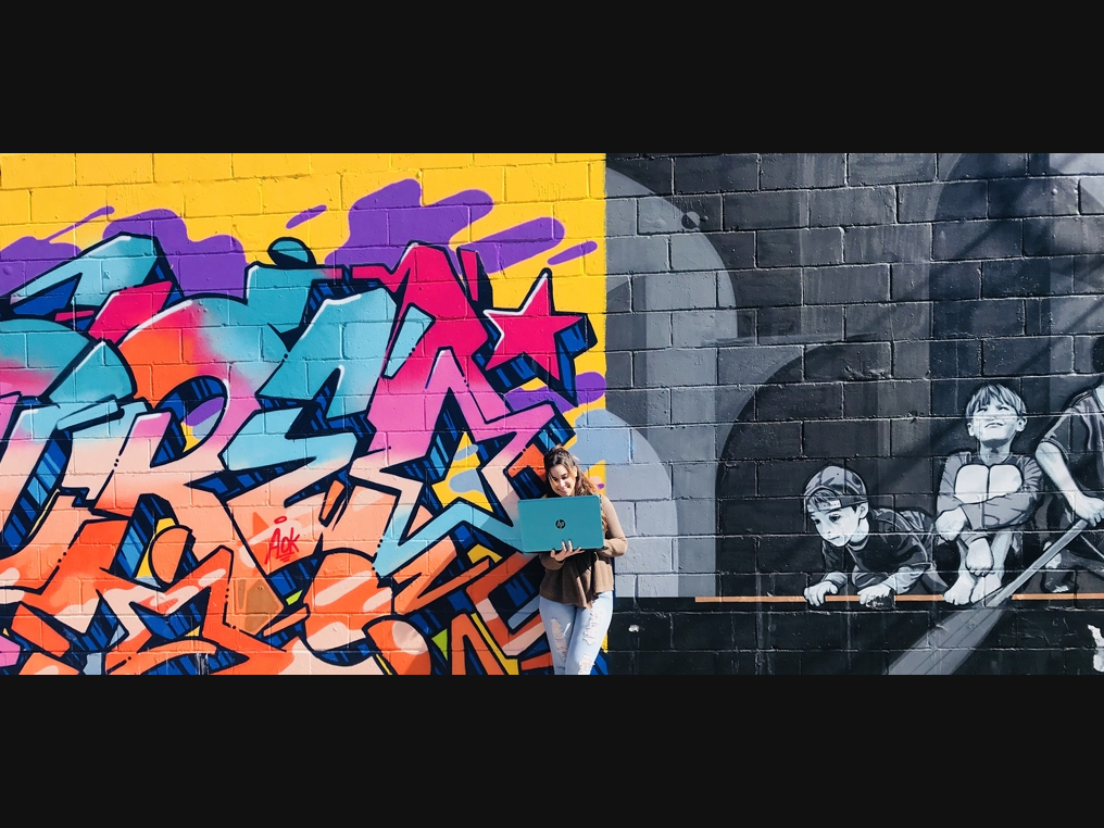 Woman on a laptop in front of a mural 