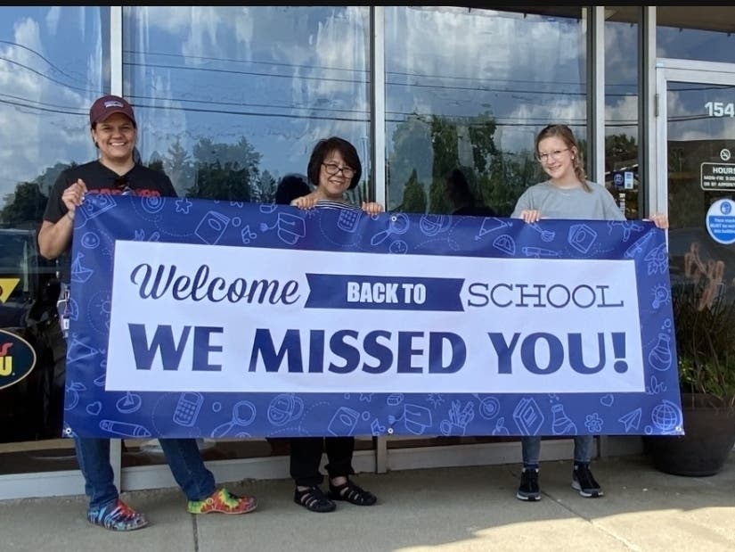 From left to right: Catherine Krick, Marlene Krick, and Violet Kirk hold a welcome back to school sign like the ones Signs Now are offering for free. 