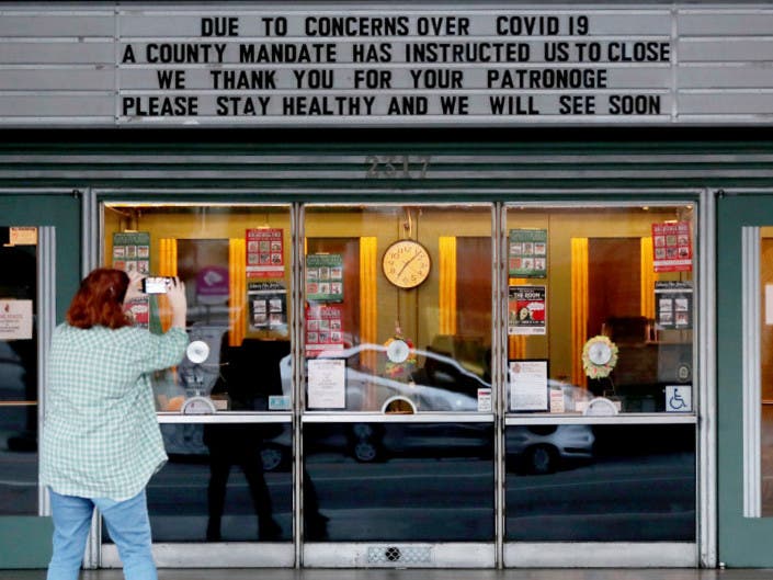 A woman takes photos of the Alameda Theater marquee in Alameda, Calif., on Tuesday, March 17, 2020. Seven Bay Area counties ordered shelter-in-place to reduce the spread of COVID-19. 