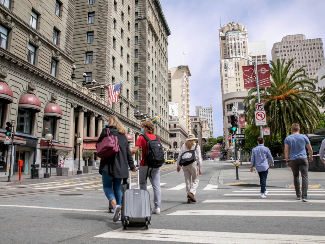 Pedestrians with suitcases walk through union square in San Francisco on June 14, 2021. The intersection of Geary and Powell Streets would have been busy with traffic, street cars and throngs of foot traffic before the pandemic. 