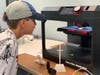 An EXCITE camper in “My Creative Space” watches his creation come to life with help from a 3D printer.