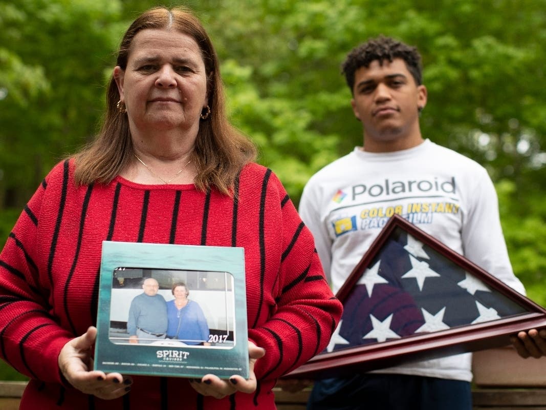 Florence Hopp, left, holds a photograph of herself and her husband Robert Hopp during a cruise in 2017, as her son J.J. Brania-Hopp holds the American flag the military presented to them after his father's death.