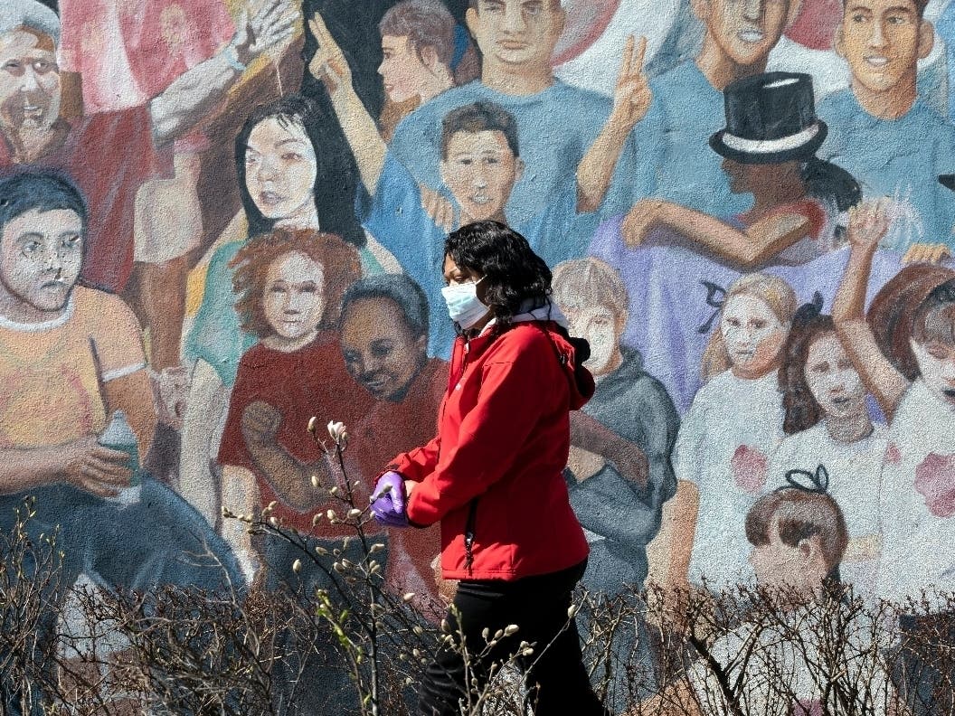 A woman wearing a surgical mask and gloves during the coronavirus outbreak walks past a mural in the Hyde Park neighborhood of Boston.