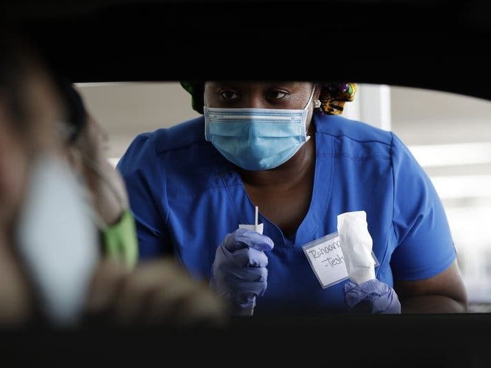 Healthcare worker Rahaana Smith instructs passengers how to use a nasal swab at a drive-thru COVID-19 testing site at the Miami-Dade County Auditorium.