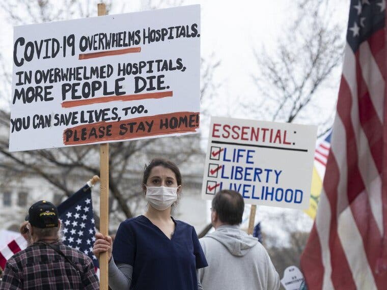 A nurse demonstrating in favor of business closures is surrounded by demonstrators against Gov. Tony Evers' restrictions on daily life due to the coronavirus pandemic.