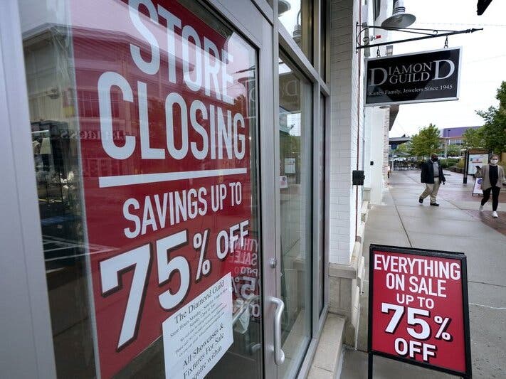 Passers-by walk past a business storefront with store closing and sale signs in Dedham, Massachusetts.