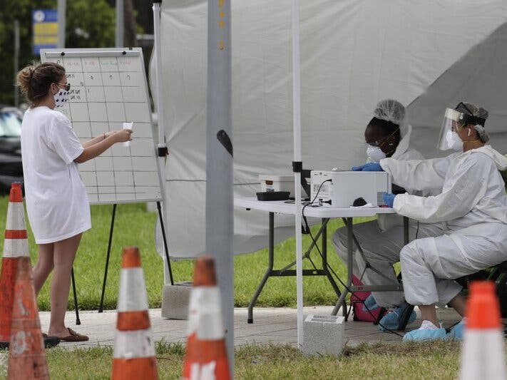 health care workers take information from people in line at a walk-up COVID-19 testing site during the coronavirus pandemic in Miami Beach, Florida.
