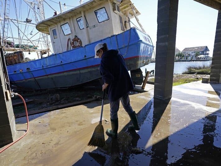 Ray Garcia sweeps water from her home Thursday after a boat washed up against it in Lakeshore, Miss. Hurricane Zeta passed through Wednesday with a tidal surge that caused the boat to become unmoored.