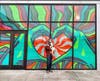 A man holds a dog in front of a mural painted by Lisa Quine in Pinecrest. 