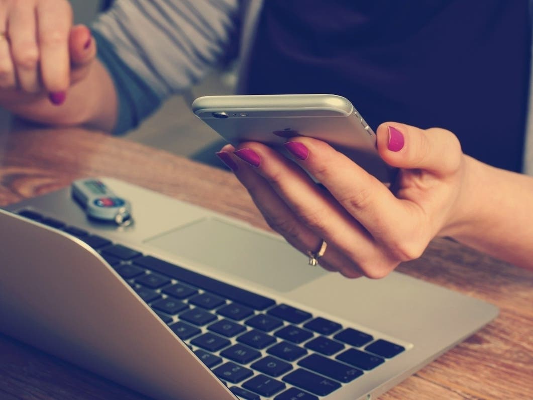 A white person holding a phone and Macbook