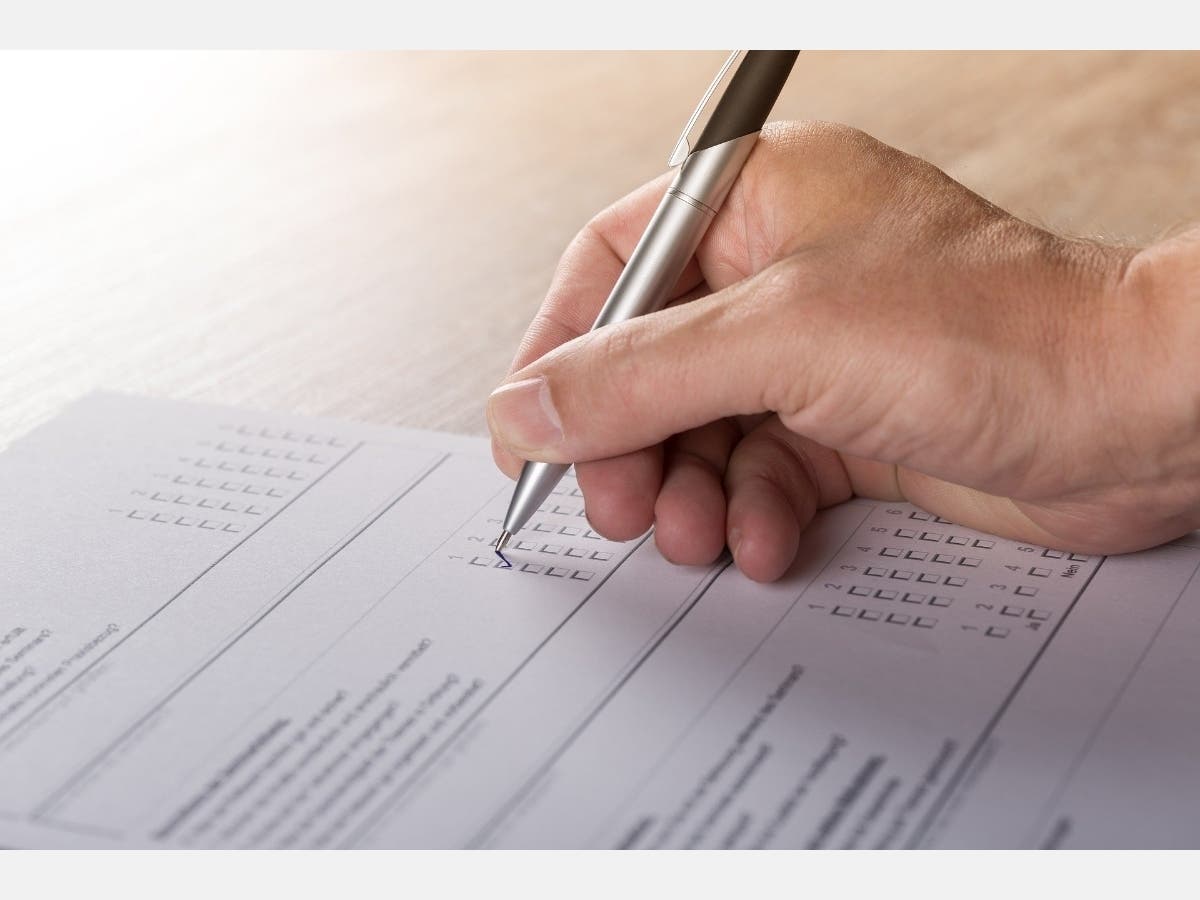 A white hand with a pen marking a ballot