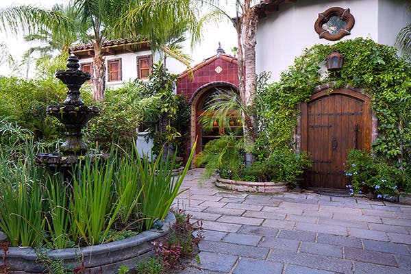 spanish style home with wood doors, red tile and large water fountain